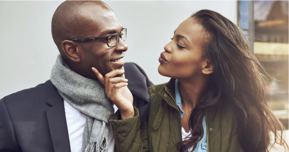 Flirting young African American woman pursing her lips for a kiss and caressing the face of a handsome man in glasses as they enjoy a date together
