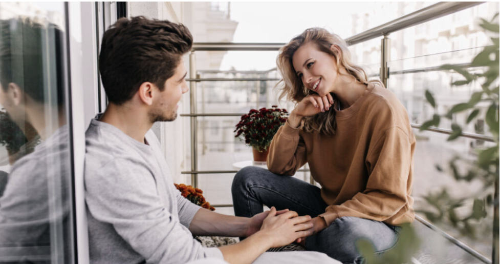 Curious caucasian girl talking with friend at terrace. Dreamy young lady sitting at balcony with boyfriend.
