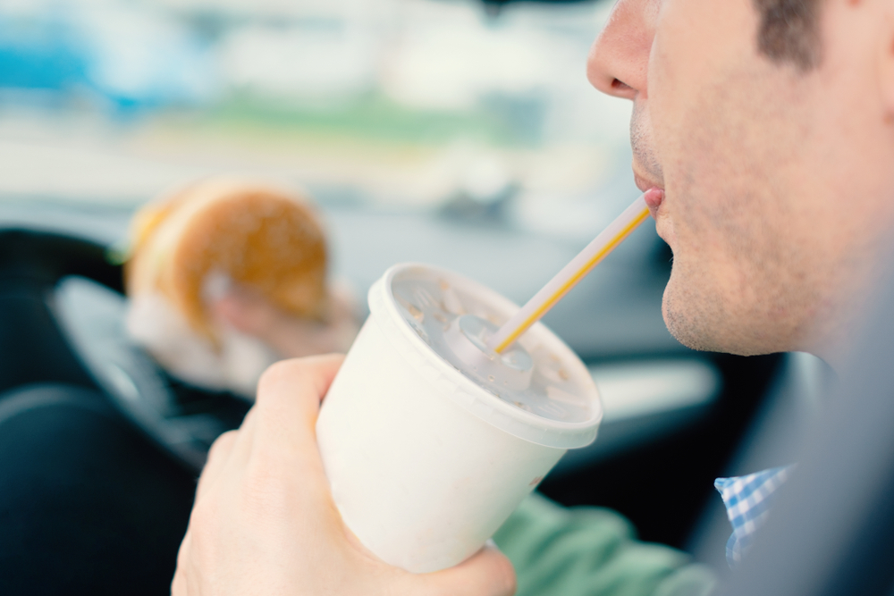 One eats junk food and cold drinking food while driving his car