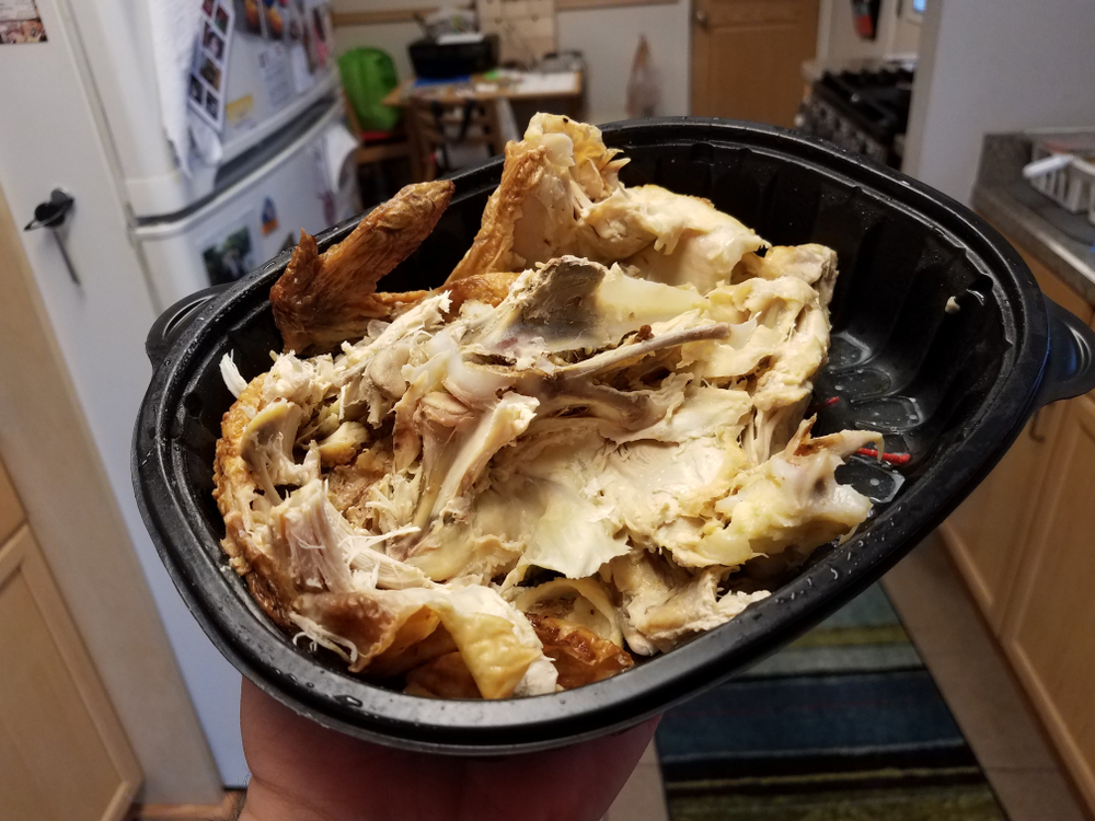 Hand holding leftover chicken in black plastic container in kitchen