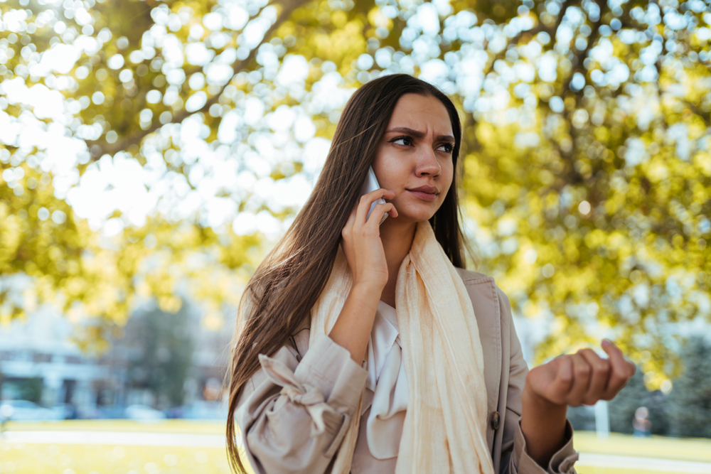 the girl listens to the phone, on her face an emotion of attention and concentration, eyebrows frowned, autumn is around
