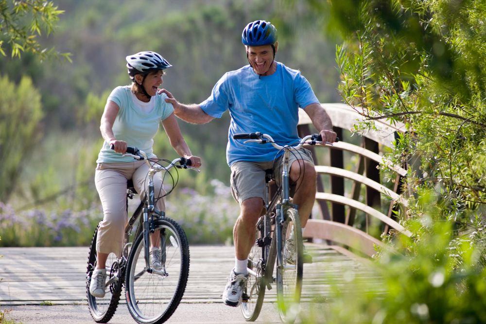 Full length portrait of an active senior couple cycling over footbridge with man leaning against woman.
