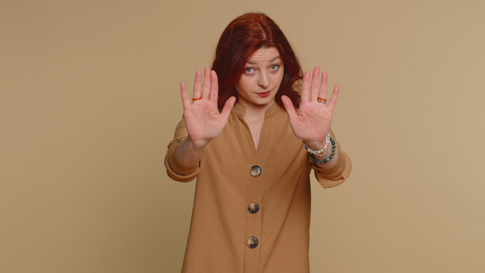 Stop. Redhead woman say No hold palm folded crossed hands in prohibited access gesture, warning of finish, declining communication, body language danger. Young girl isolated on beige studio background