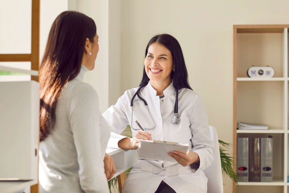 Portrait of smiling doctor wearing stethoscope holding report file with appointment and giving consultation a woman sitting back and listening to doctor during medical examination in clinic.