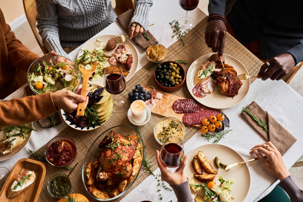 Top view of group of diverse friends enjoying homemade food at dinner table with turkey or chicken, copy space