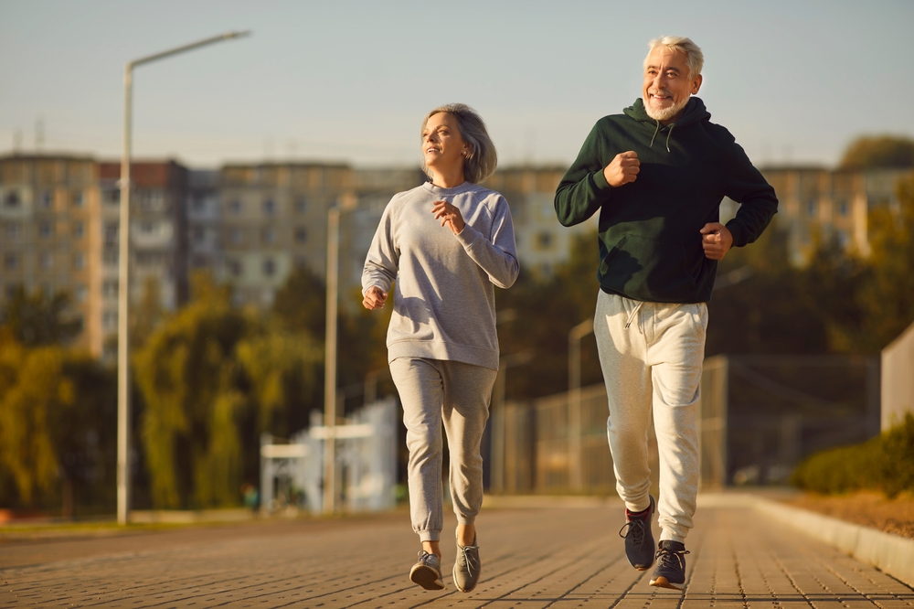Senior people having an active outdoor workout. Married older adult couple jogging on a nice summer morning. Happy healthy old husband and wife in sports clothes running along the pavement together