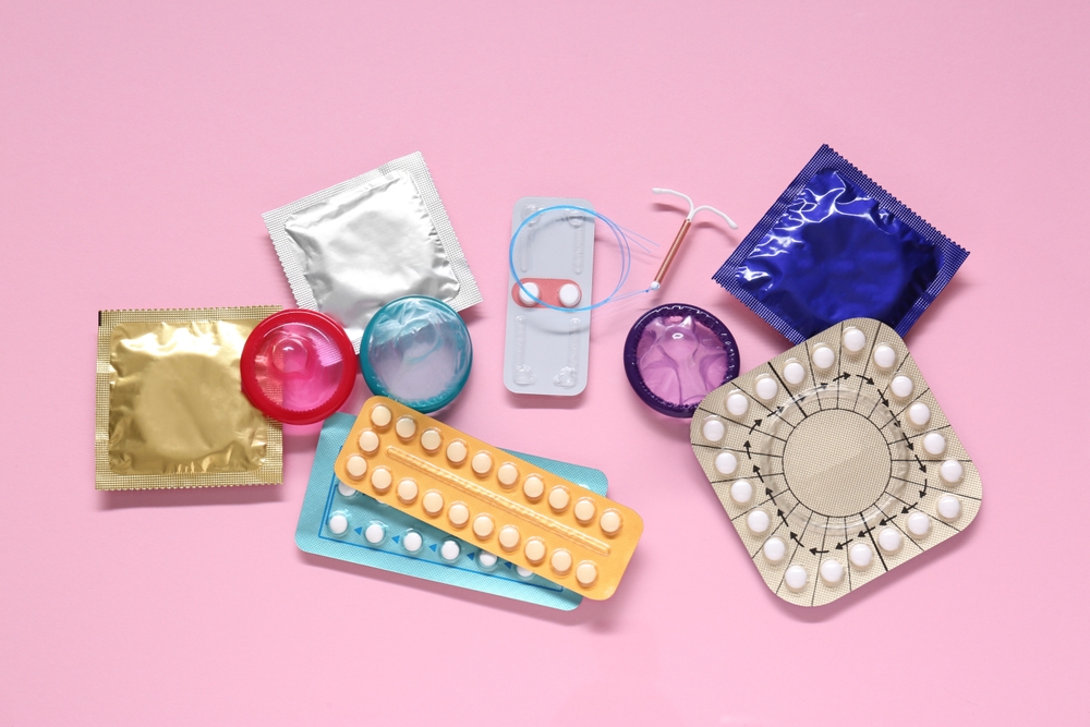 Contraceptive pills, condoms and intrauterine device on pink background, flat lay. Different birth control methods