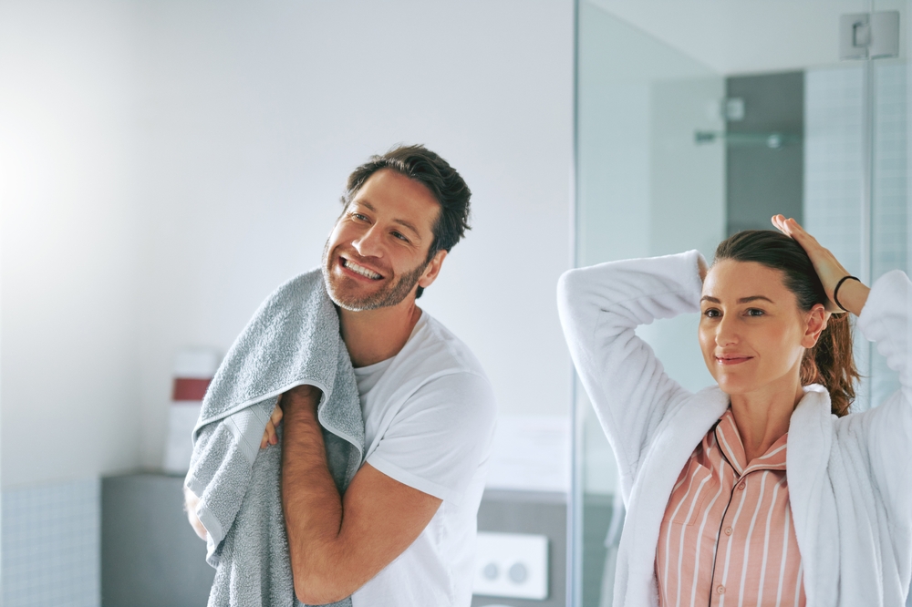 Couple, getting ready and happy in bathroom for morning routine with skincare, grooming and haircare in home. People, smile or cosmetics with hygiene preparation, start of day or wellness for wake up