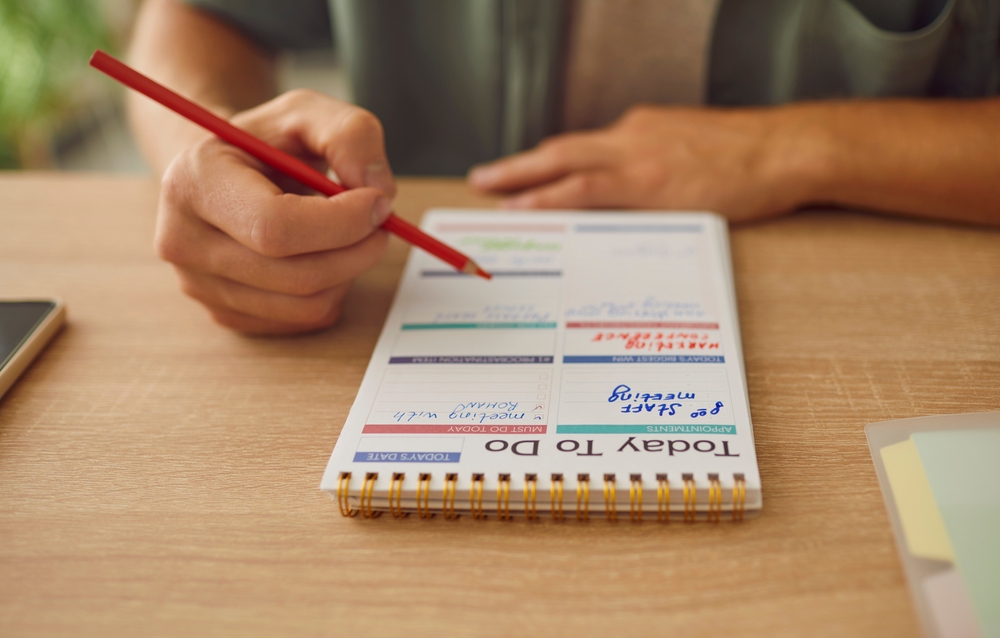 Hands write a detailed plan, schedule, and task list in a notebook. His actions revealed a commitment to planning, using calendar pages as a canvas for organizing daily activities.