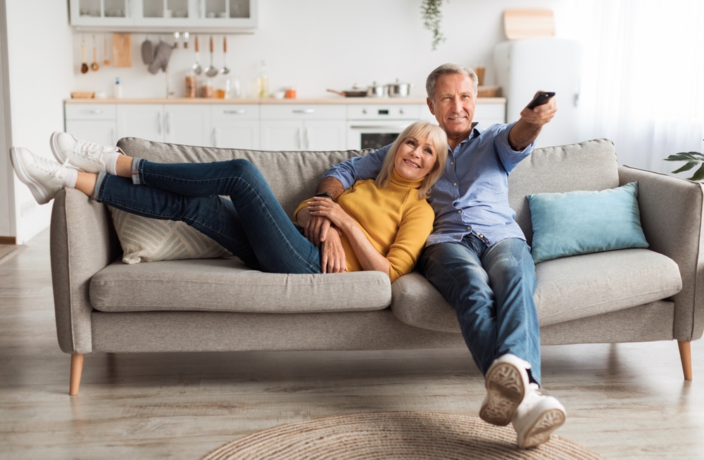 Relaxed Senior Couple Watching Television Together Sitting On Sofa And Pointing Remote Controller Switching Channels Relaxing At Home On Weekend. TV Programming Concept