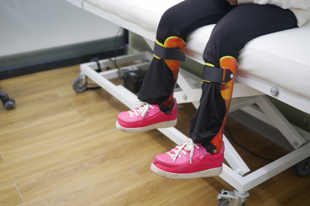 Child's Legs With Orthopedic Braces and Bright Pink Shoes on Clinic Bed