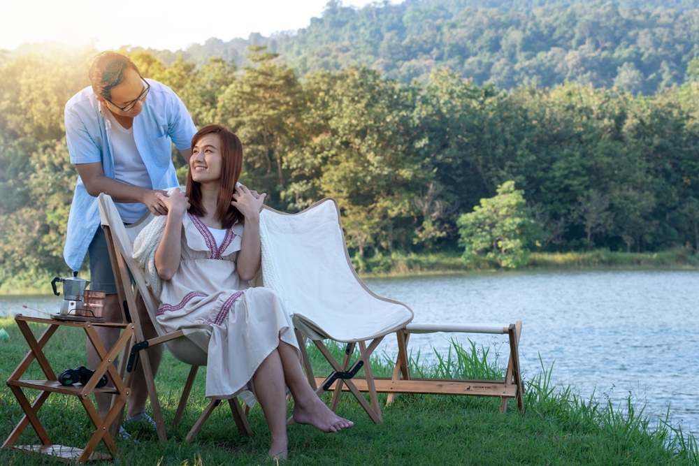 Couple enjoying time together outdoors, man takes care of a woman by putting blanket on her shoulders, while she relaxes and enjoys nature