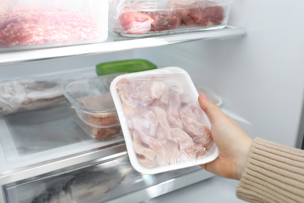 A woman takes frozen chicken from the freezer, nearby