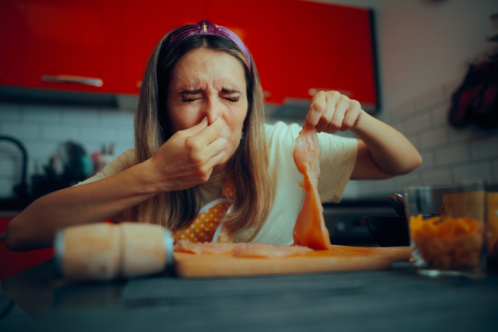 Cooking The woman holding the meat is confused by the person who smells it and feels put off by the chicken meat going bad at home