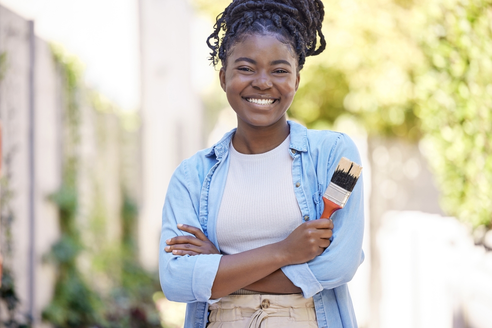 Portrait, painter and smile of black woman for renovation, design or diy maintenance repair. Arms crossed, painting tools and confident person with brush outdoor for remodeling or decor in Nigeria