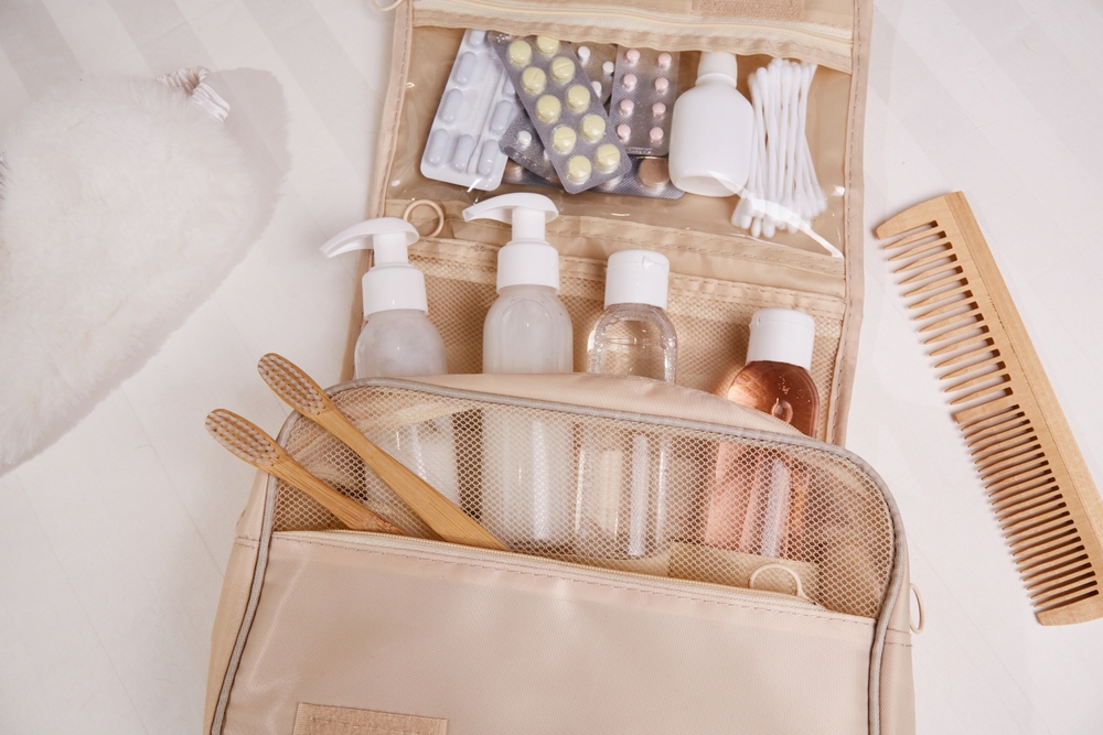 Travel set of toiletries on white bed linen. The organizer contains personal hygiene items, cosmetic bottles , toothbrushes, pills, necessary for traveling.