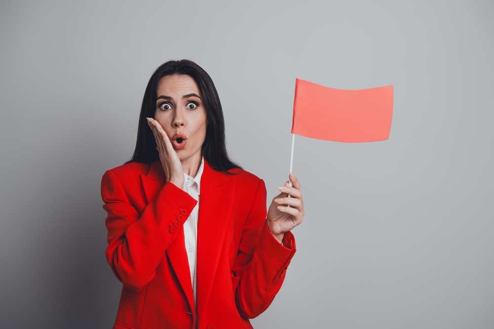 Confident businesswoman holding a red flag with a surprised expression concept for caution or warning