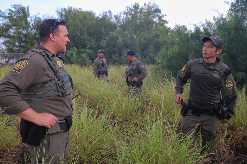 McAllen, TX, U.S.A.- Aug. 26, 2025: Two Border Patrol agents with DPS troopers in high grass discuss a search for three migrants who entered the U.S. illegally by crossing the Rio Grande River.