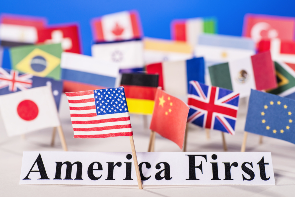 The American flag is in front of the Slogan America first and many other countries' flags.