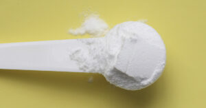 Close up, scoop of powdered creatine monohydrate with yellow background