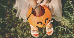 Two Candy Bars Recalled Before Halloween Over Dangerous Ingredient Girl reaching into plastic halloween pumpkin bucket for trick or treating