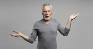 Caucasian handsome surprised gray haired bearded senior man 60 years old, holding his hands palms up, looking at camera with amazement, posing over grey isolated background with free advertising space