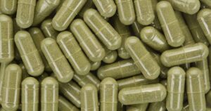 Capsules containing green powder. Natural supplement concept