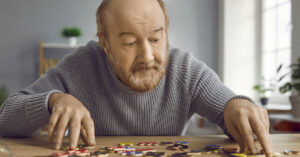 Study Reveals How Alzheimer’s Progression Could Be Stopped Long Before Symptoms Start eldery man doing a puzzle. Mental sharpness, mental health and dementia concept