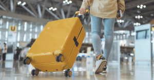 Person walking through airport pulling a yellow piece of luggage behind them