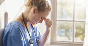 Trump Plan to Remove Nursing from Professional Degrees Draws Backlash Tired nurse with fingers pinching bridge of nose due to exhaustion