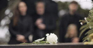 21-Year-Old Student Dies Days After Mistaking Illness for Just a ‘Bad Virus’ White rose placed on casket at funeral. Attendees seen in background out of focus