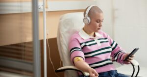 Why Millennials Are Facing Higher Cancer Rates Than Previous Generations Higher cancer rates millennials concept showing a young person undergoing cancer treatment and using a smartphone.