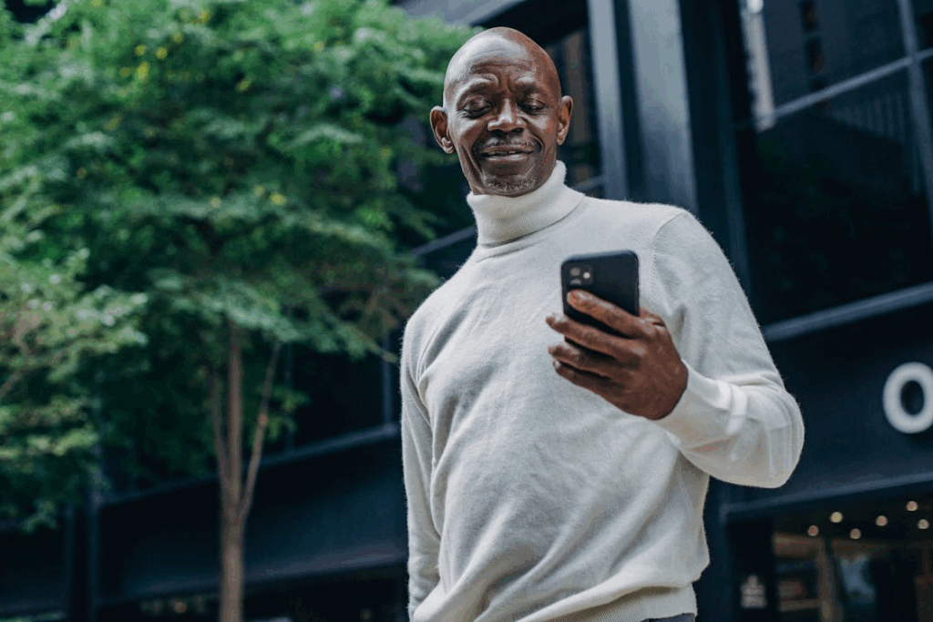 Cheerful black man browsing smartphone on street signs of success
