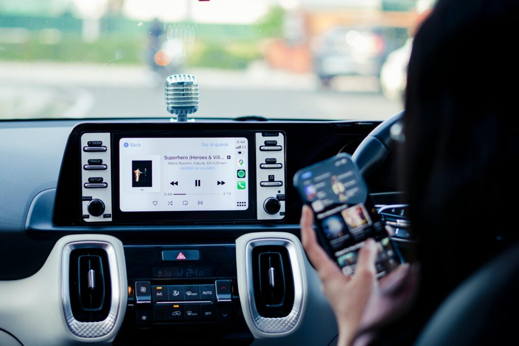 A driver selects music on a car's touchscreen display while holding a smartphone.