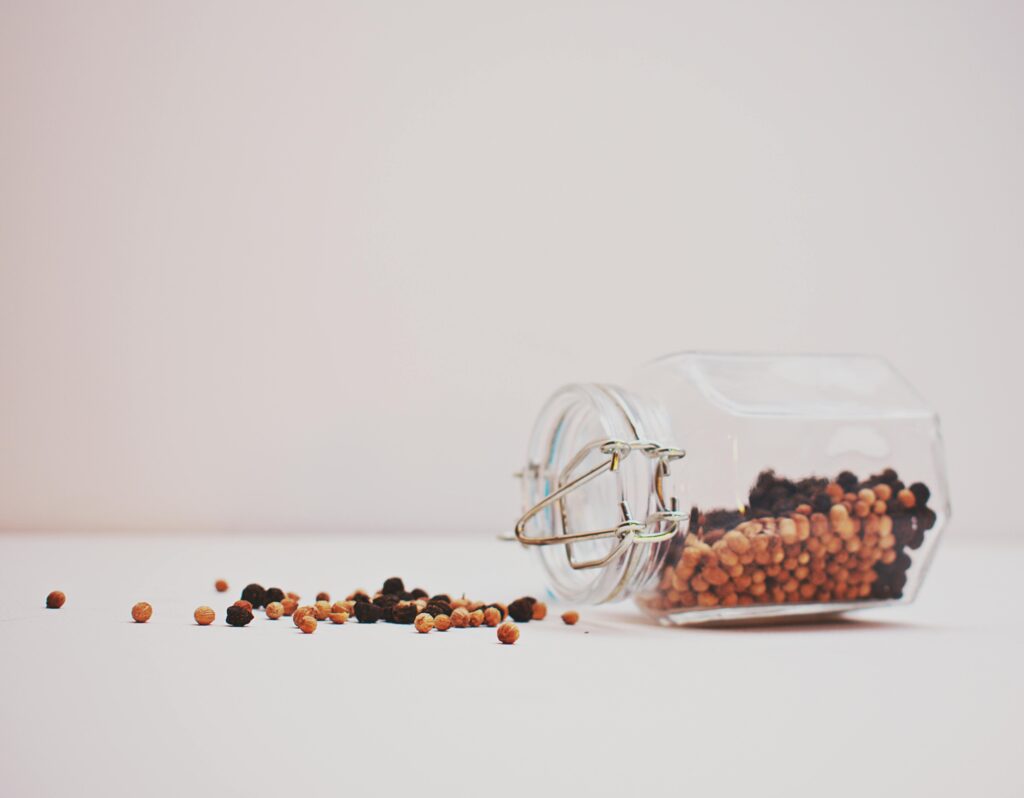 Black and Brown Peppercorns Spilling from Glass Jar

