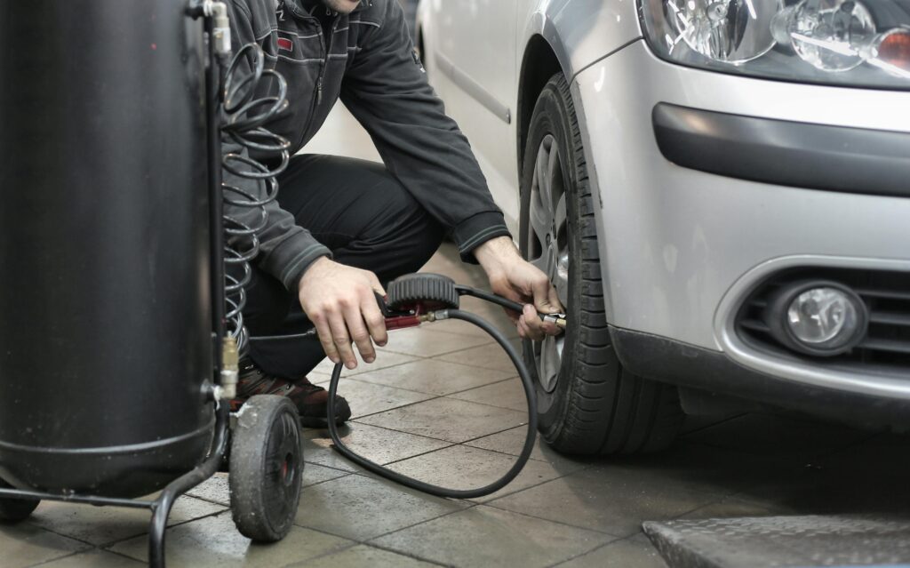 Man in Black Jacket and Black Pants Sitting Near Silver Vehicle.