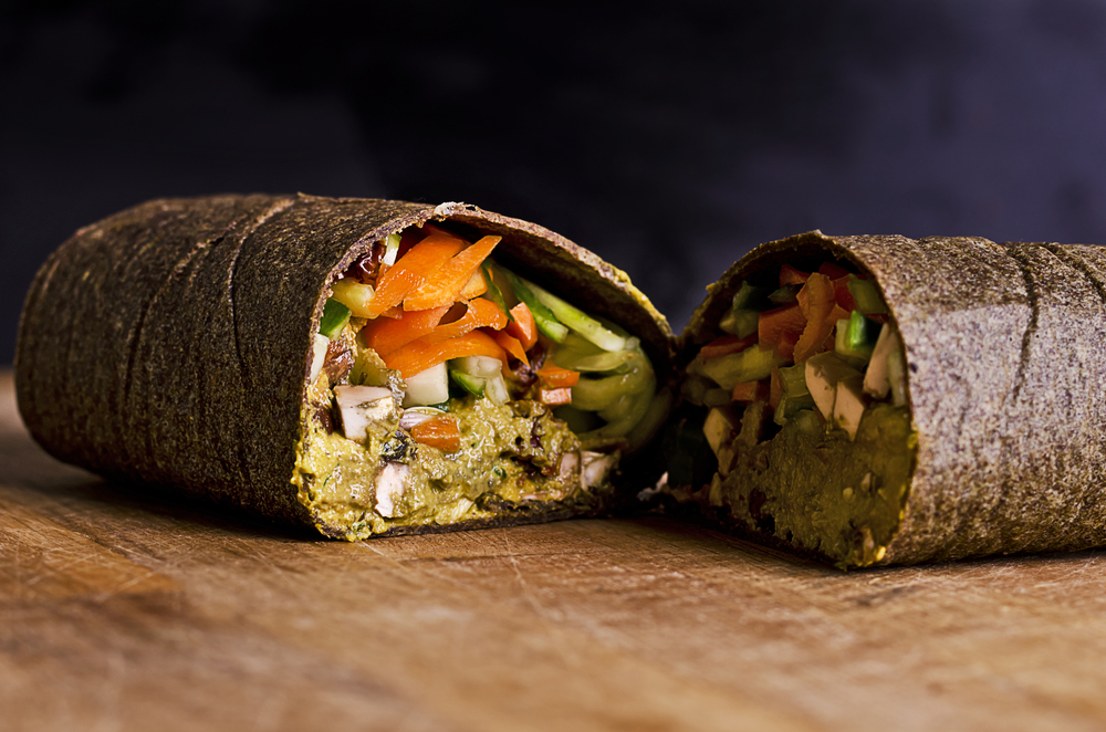 sliced up raw food wrap with vegan ingredients and green pesto on a wooden plate