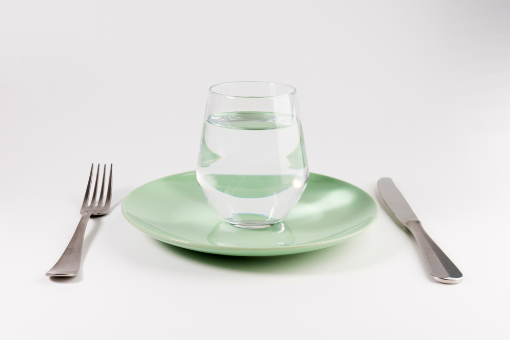 glass of water in a plate with knife and fork isolated on white background