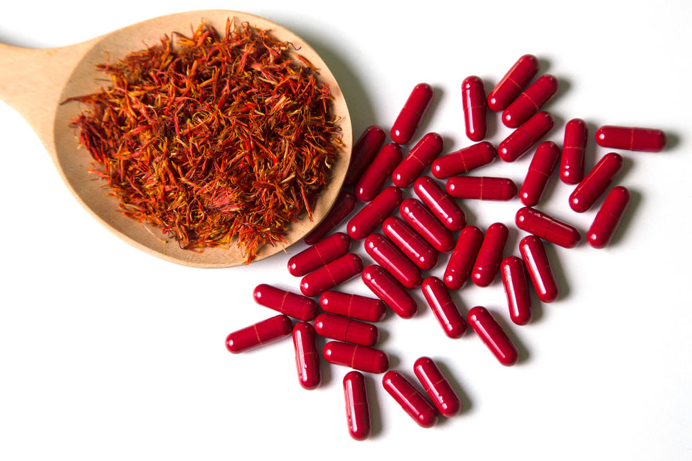 Red capsule pills and Safflower, False Saffron, Saffron Thistle in wooden spoon on white background.