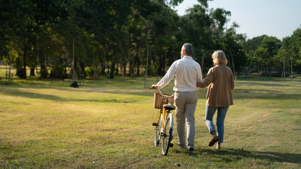 Caucasian elderly couples walking with a bicycle in the natural autumn sunlight garden feel cherish and love, concept elderly love, warm family, Happier Old-Age, retirement lifestyle.