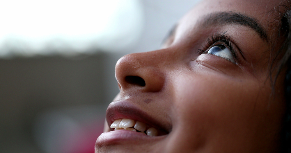 African descent girl looking up with HOPE and FAITH. Happy preteen child eye