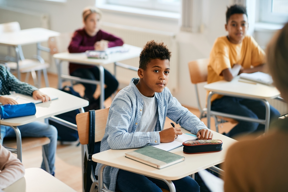 Black schoolboy paying attention and taking notes during a class at elementary school.