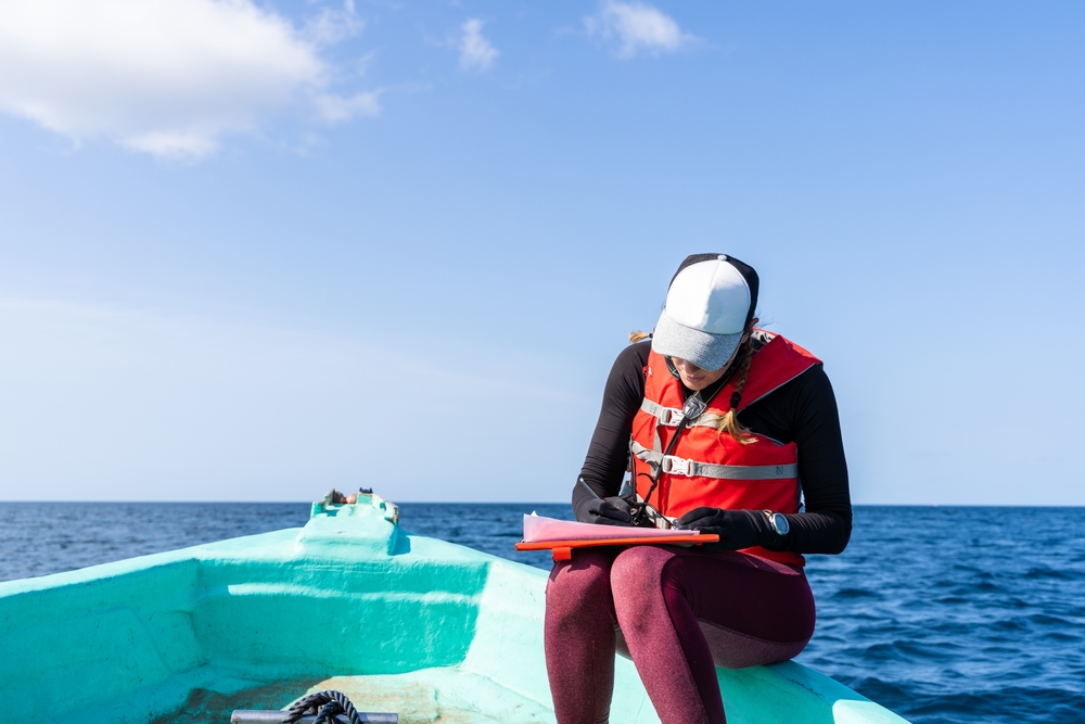 Marine biologist writing down data sitting on top of a boat in the middle of the sea