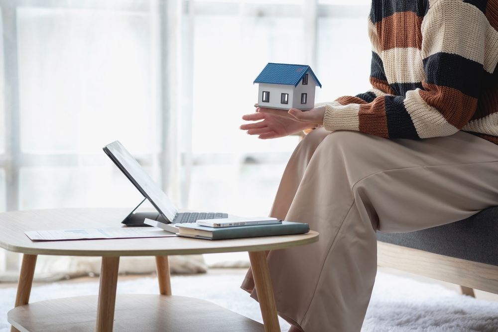 Young Asian woman calculating the cost of selling a house and analyzing the return on real estate investments. Real estate accounting concepts and tax system.