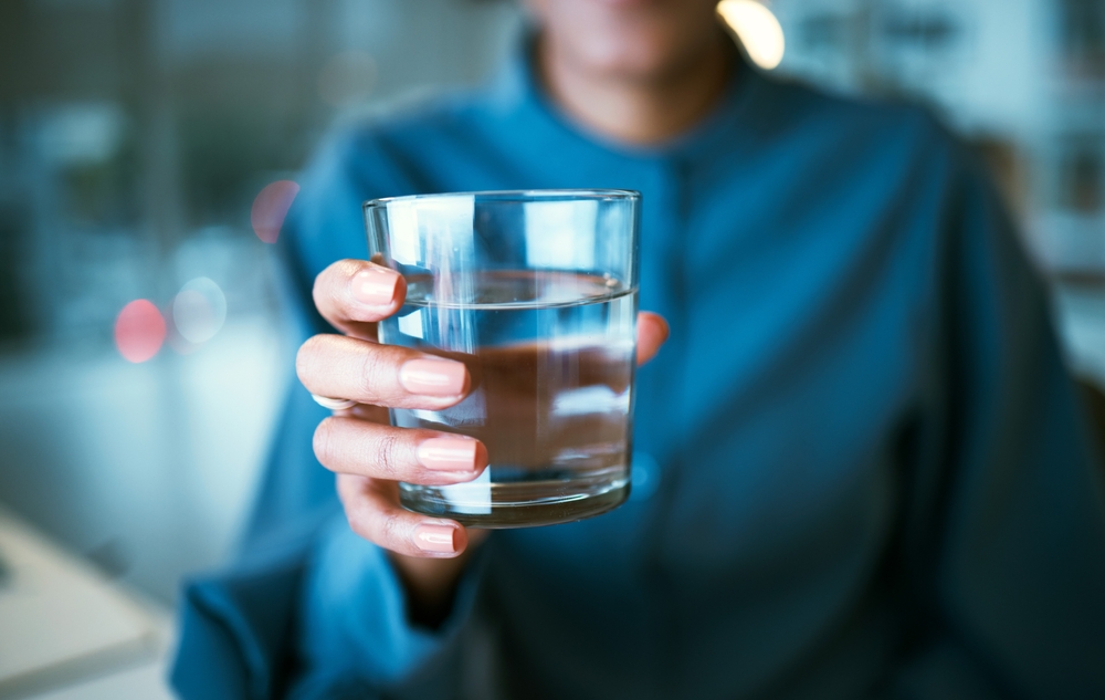 Water, glass and hand closeup in office, woman and giving for hydration, wellness or choice at finance company. Accountant, natural drink and zoom for nutrition, diet or detox for health in workplace