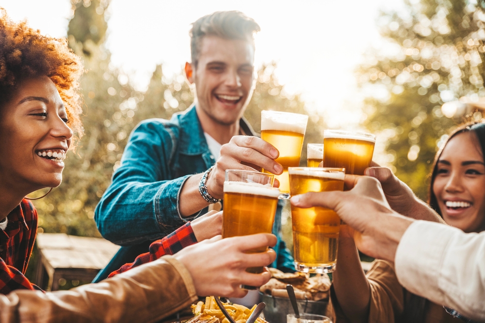 Multiracial group of friends having dinner together - Diverse young people sitting at the Blass Glant Bar table in the Brewery Pub Garden - happy hour, lunch break and rest break
