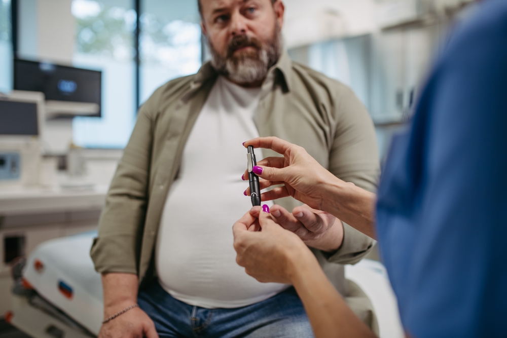 Nurse checking man's blood glucose level using a fingerstick glucose meter. Obese, overweight man is at risk of developing type 2 diabetes. Concept of health risks of overwight and obesity.