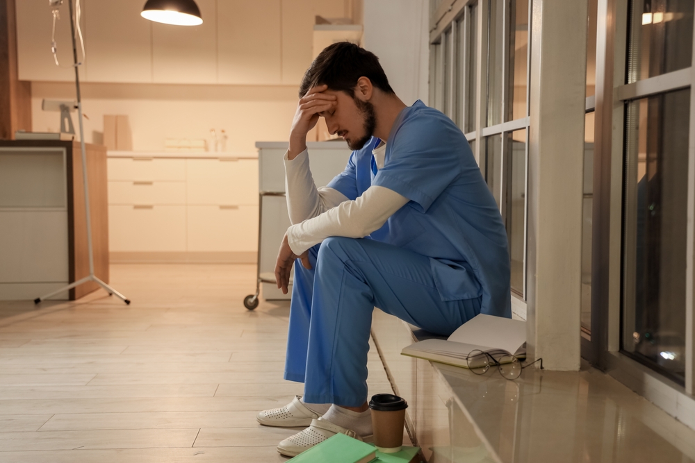 Tired male nurse sitting on windowsill at hospital in evening