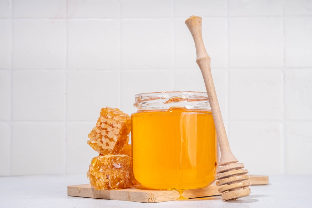 Golden honey in a small pot, with a spoonful of beeswax and honey 