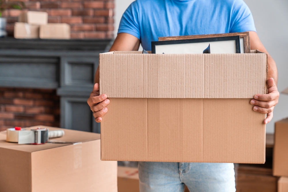 Cropped image of man carrying boxes full of stuff moving in new house. Young guy with box indoors. Moving into new home. Relocate, rental, rent, delivery, relocation and unpacking concept